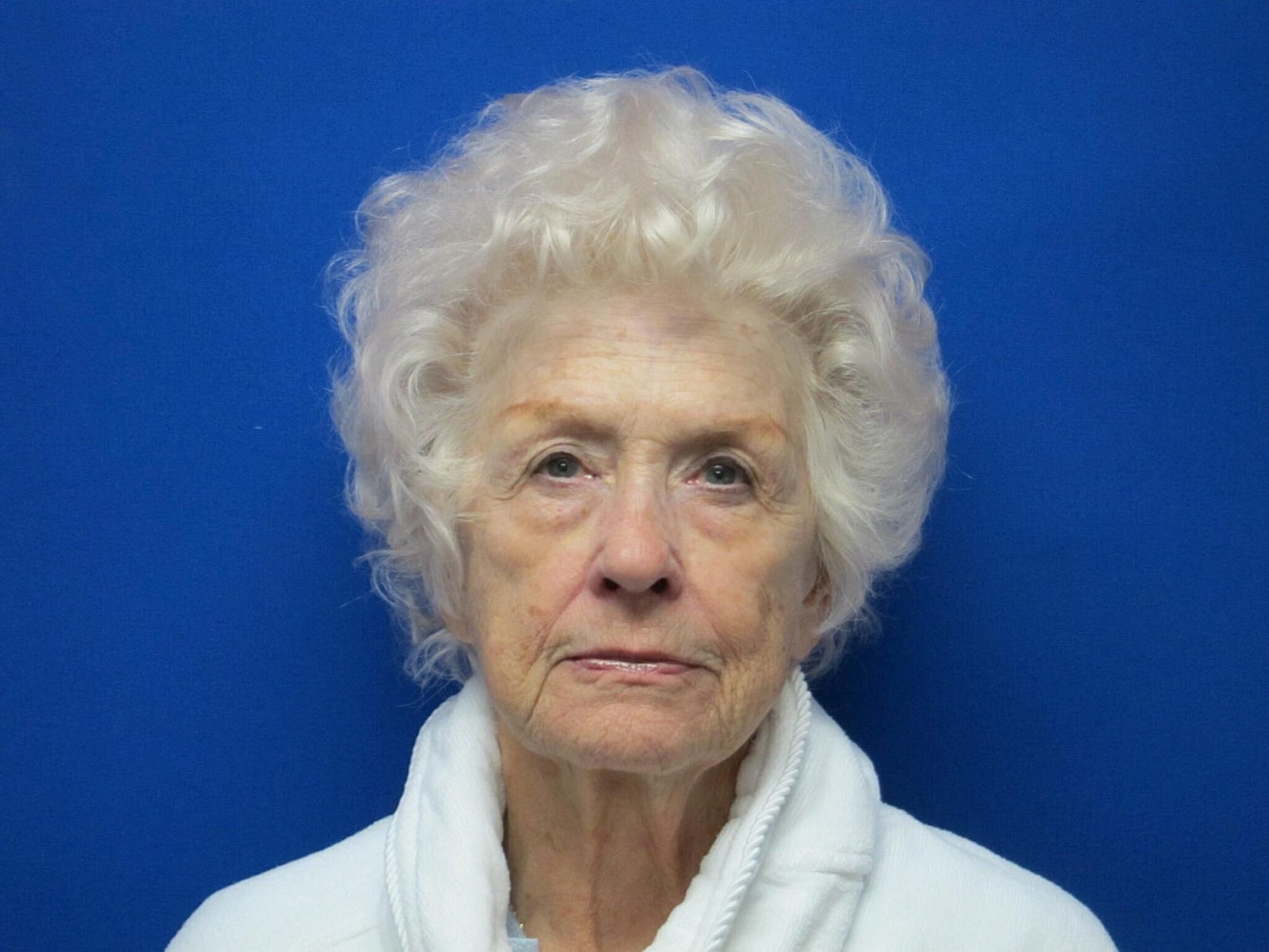Elderly woman with curly hair against blue background.