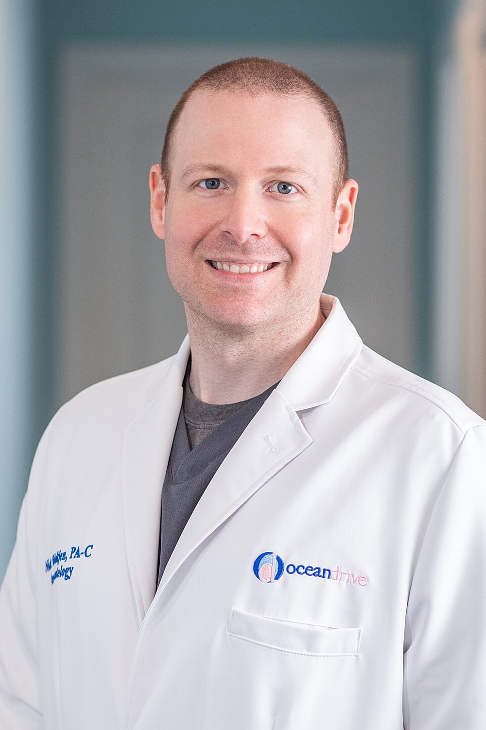 Male physician in white coat smiling at camera.