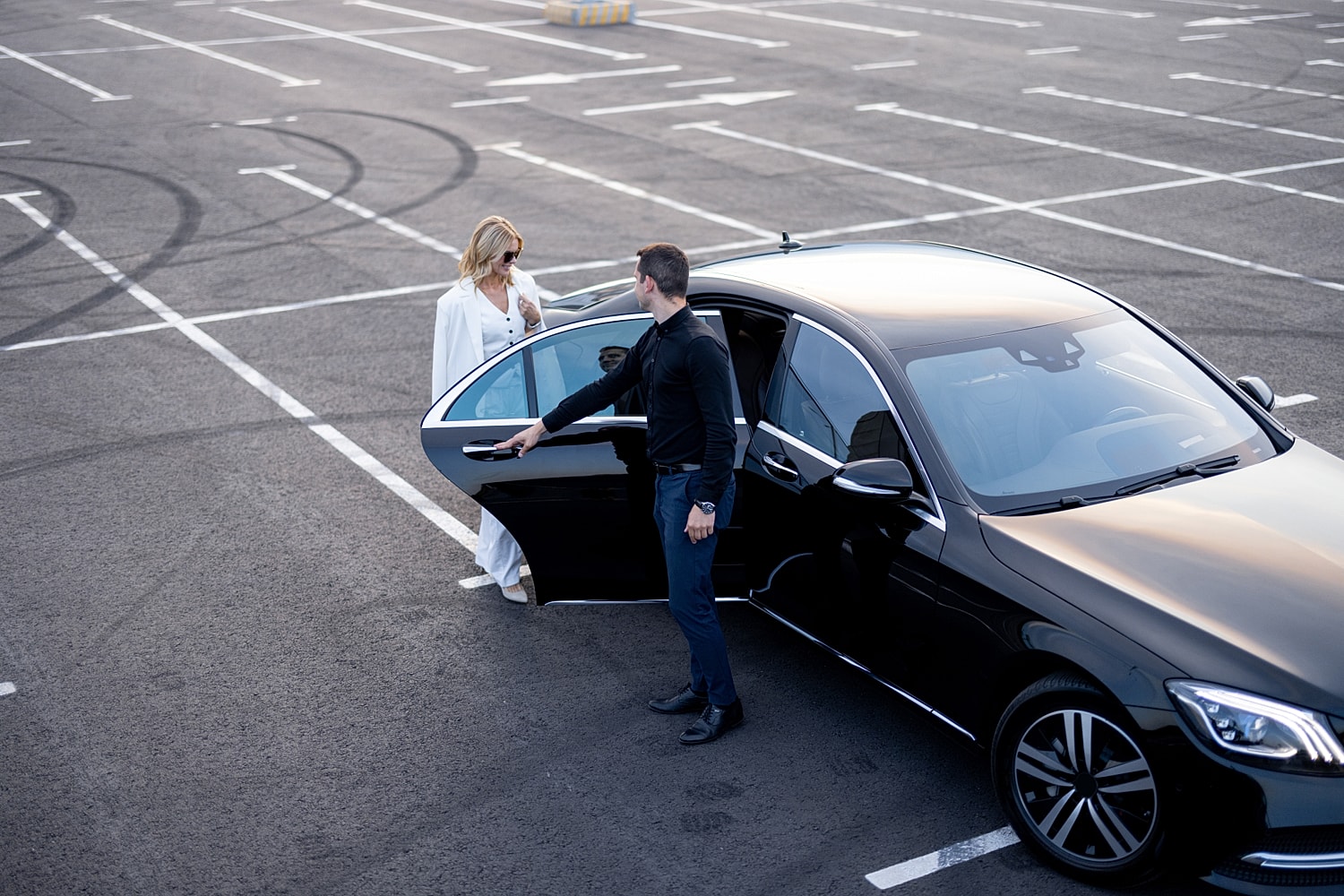 Man opening car door for woman in parking lot.