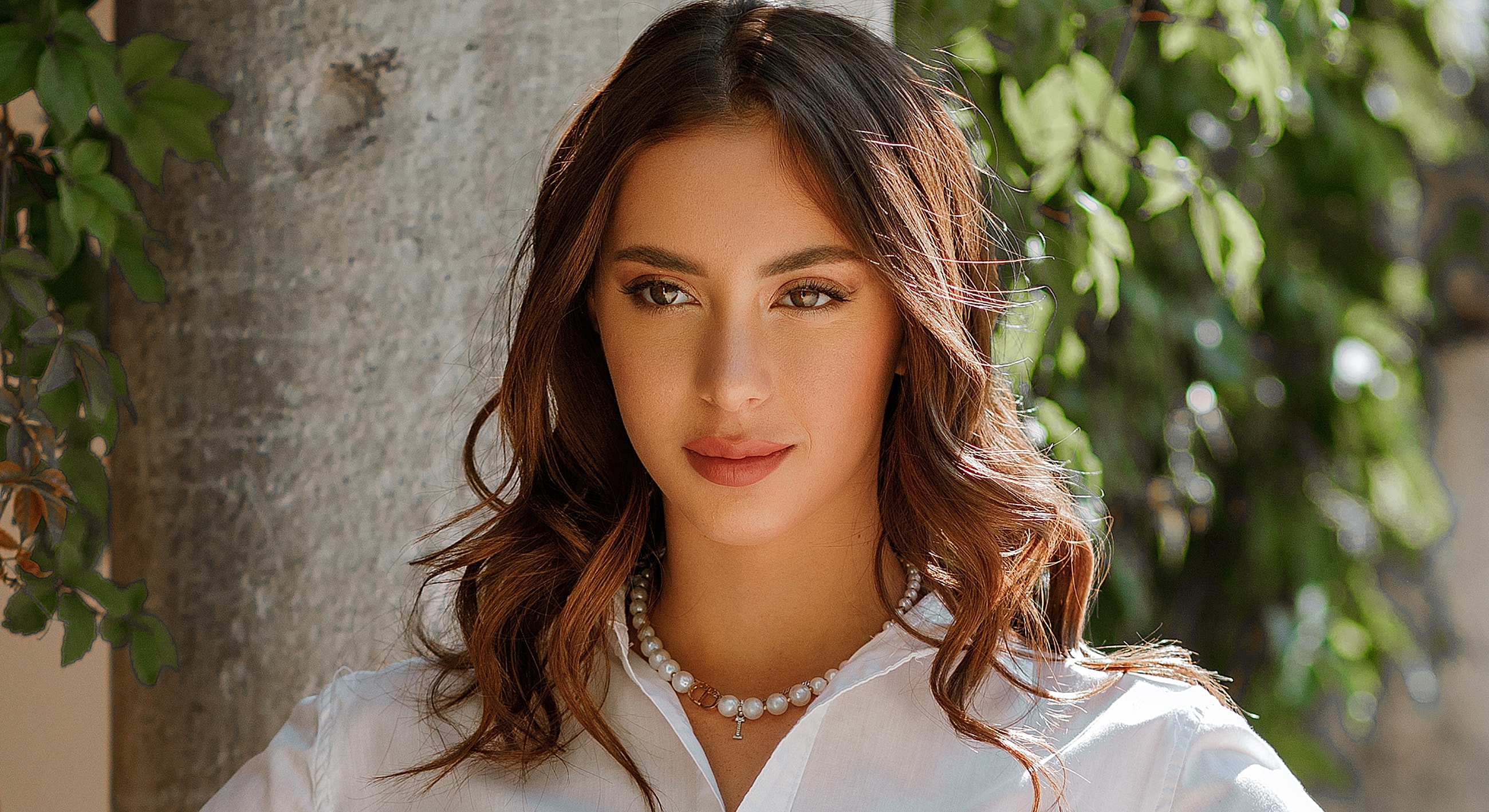 Woman outdoors with elegant necklace and soft smile.